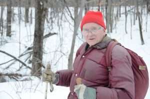 A man wearing winter coat and hat standing in a snow-covered forest